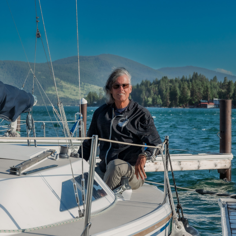 Person in sunglasses on a boat by a lake with mountains in the background.