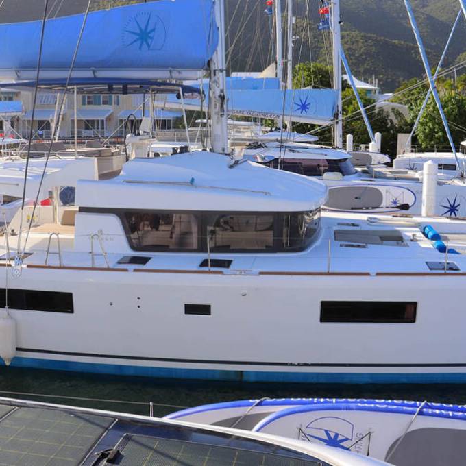 White catamaran named Happy Ours docked in a marina with blue sails.