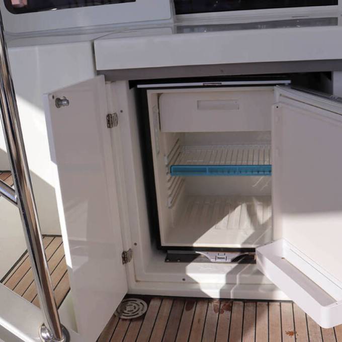Open mini fridge in boat interior near wooden stairs.