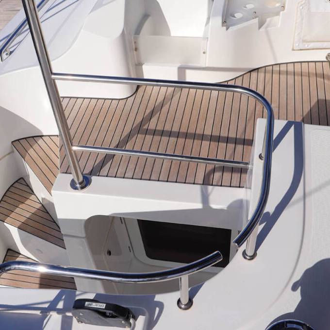 Boat deck with wooden flooring, stainless steel railings, and an open hatch.