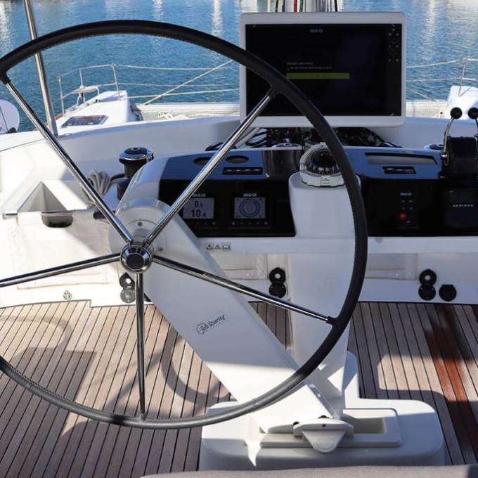 Yacht helm station with a steering wheel, navigation screens, and water background.