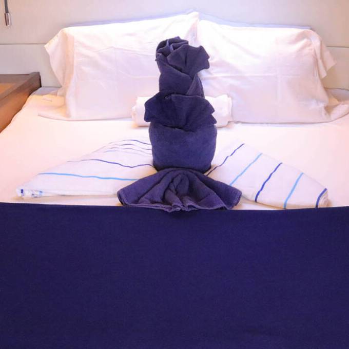 Neatly arranged bed with folded towels shaped like a person, blue and striped towels, white pillows.
