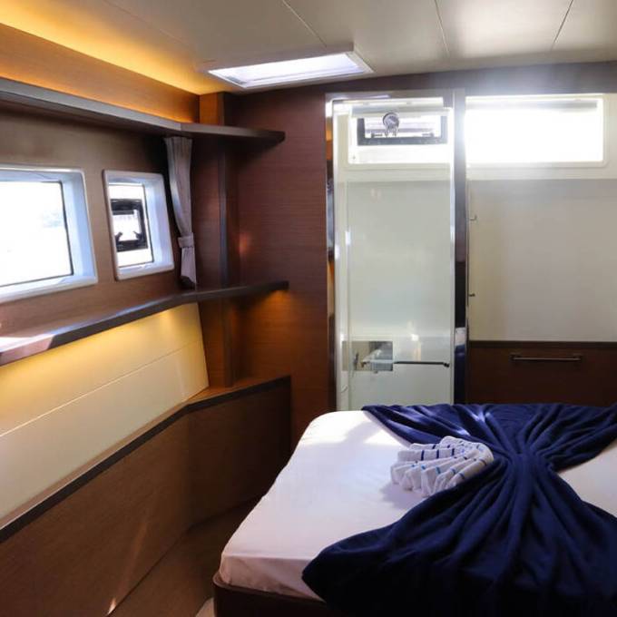 Interior of a cozy cabin with a bed, windows, shelves, and a glass door leading to a bathroom.
