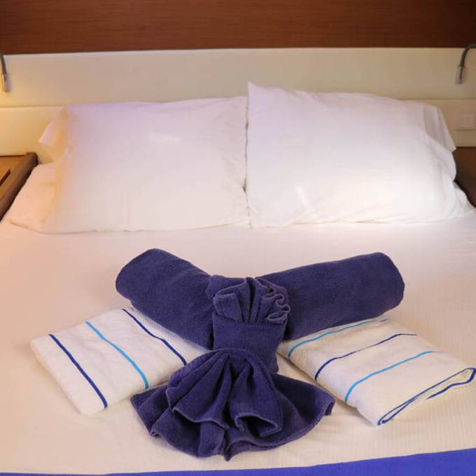 Neatly made bed with white pillows and folded blue and white towels on top.