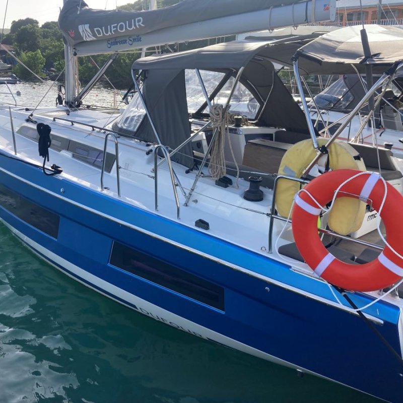 Blue and white sailboat docked, with a red lifebuoy attached to the side.
