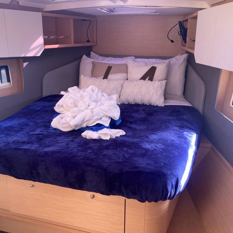 Cozy boat cabin with a bed, blue blanket, and white pillows, lit by natural light from window.