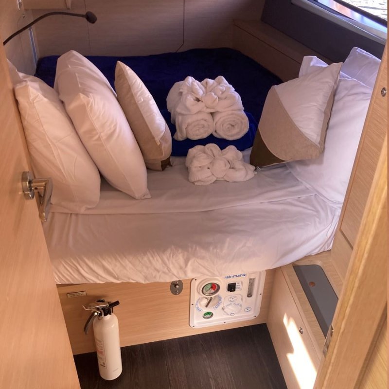 Small boat cabin with bed, pillows, rolled towels, and fire extinguisher.
