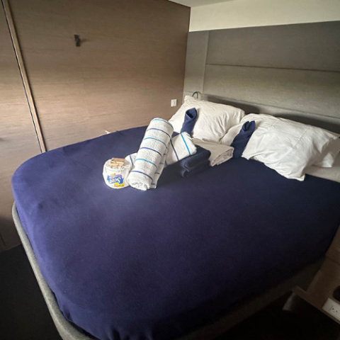 Bed with navy bedding, rolled towels, and a snack pack on top in a cozy room.