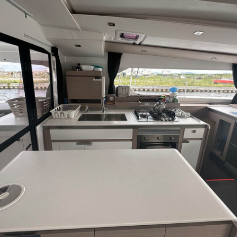 Interior view of a yacht kitchen with appliances and a window showing outside scenery.