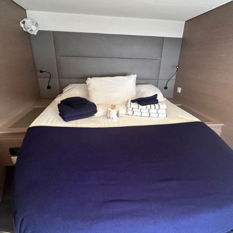 Neatly made bed with folded towels and dark blue bedding, small table lamps on each side.