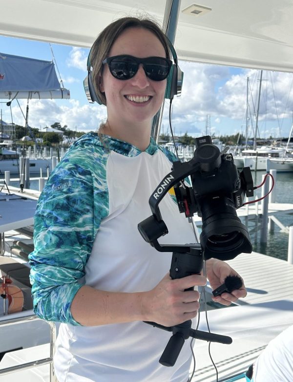 Alexandra Kozub smiling, holding camera equipment, with marina in the background.