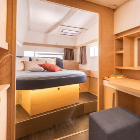 Cozy boat cabin with bed, cushions, shelves, and a small desk area.