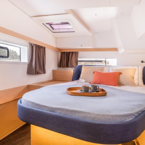 Cozy cabin with a bed, pillows, curtains, and a tray with mugs and a glass bottle on a boat.