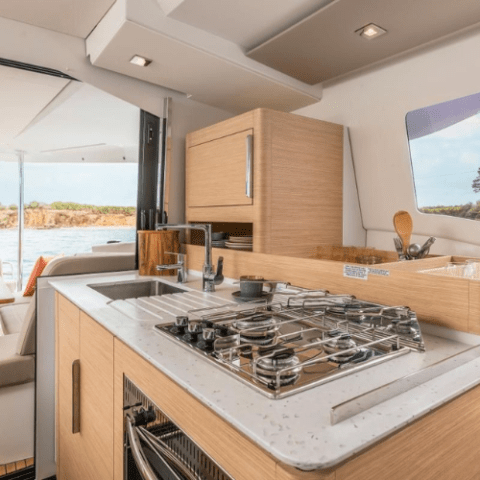 Interior of a boat kitchen with a stove, sink, and wooden cabinets overlooking water.
