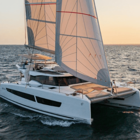 Sailing catamaran with white sails on open water at sunset.