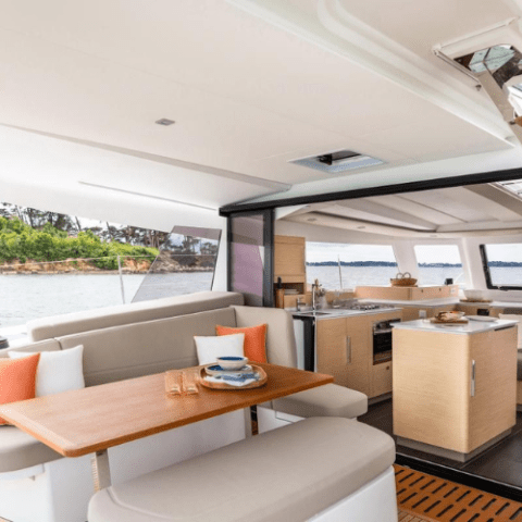 Interior of a yacht with a dining area and kitchen, overlooking the sea.