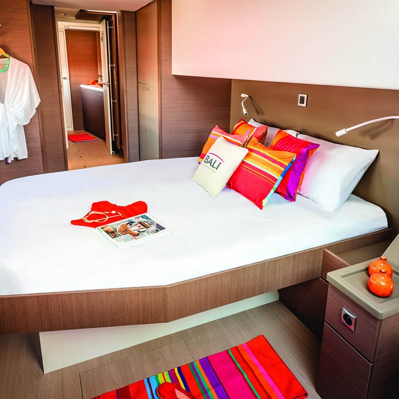 Modern bedroom on a boat with a neatly made bed, colorful pillows, and a robe hanging on the wall.