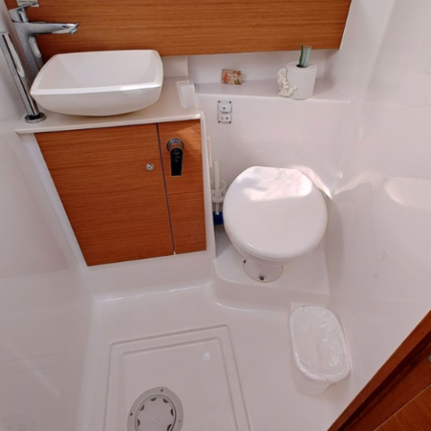 Compact boat bathroom with toilet, sink, and wooden cabinet.