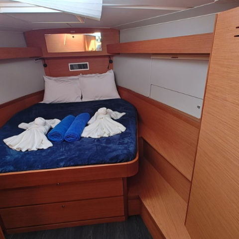 Boat cabin with a double bed, blue bedding, towels, and wooden interior.