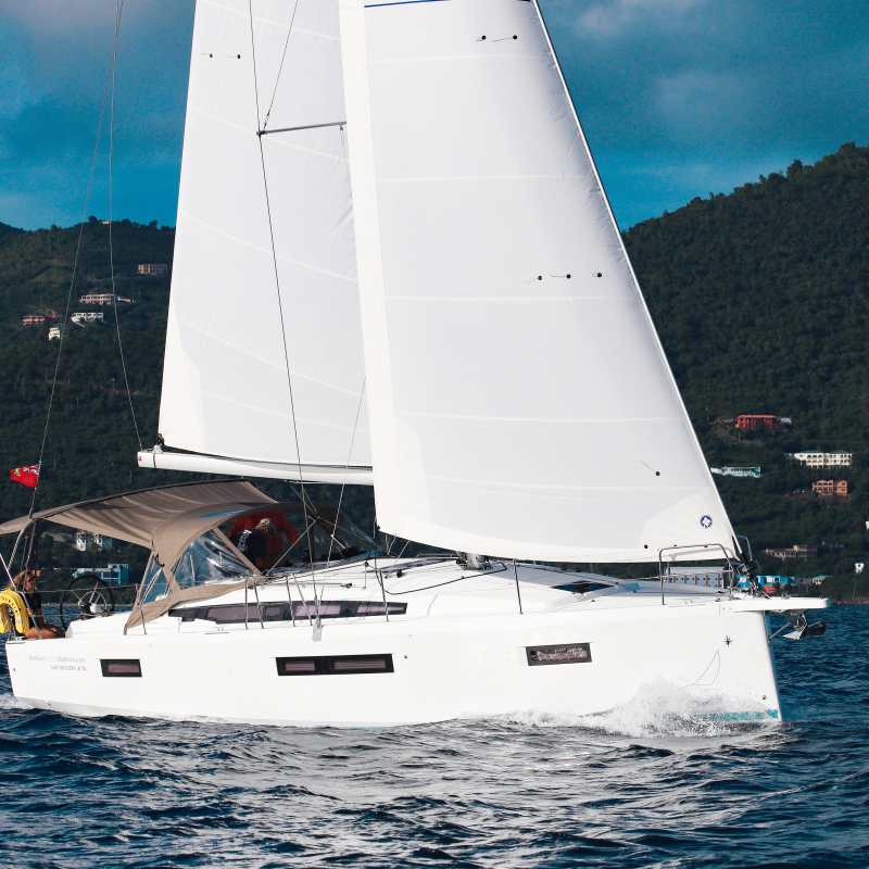Sailboat with white sails on the water, green hills in the background.