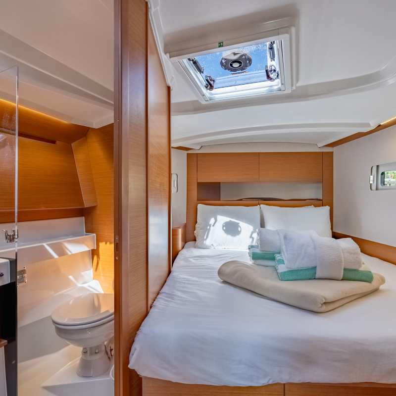 Cozy boat cabin with a neatly made bed, wooden accents, and small bathroom.